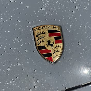 Water beading on grey paintwork around a Porsche crest.