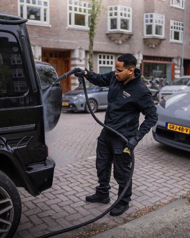 A SPOTWASH detailer rinsing a car on an Amsterdam street.